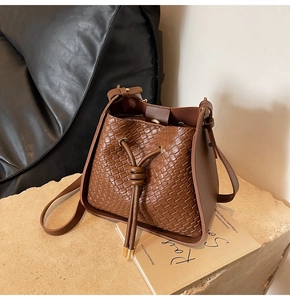 Close-up of brown woven bucket bag with drawstring closure on a stone pedestal