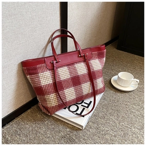 Detail of red and white plaid canvas tote bag with leather straps on a white table