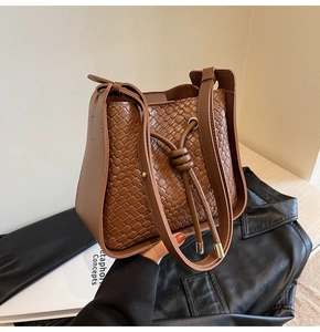 Detail of brown woven leather bucket bag featuring drawstring closure and shoulder strap