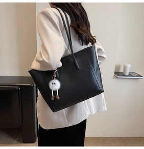 Detail view of large black tote bag featuring a cute plush character charm on shoulder