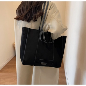 Large black tote bag with white contrast stitching worn by a model in a warm hallway
