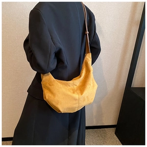 Détail d'un sac hobo en daim jaune gingembre porté avec un blazer noir au style minimaliste