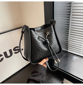 Detail of black woven bucket bag showing intricate cross-weave texture and golden cord ends