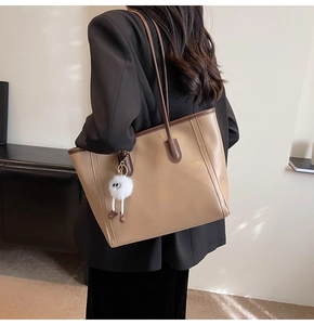 Detail view of large faux leather tote bag with brown trim and plush charm hanging on the side