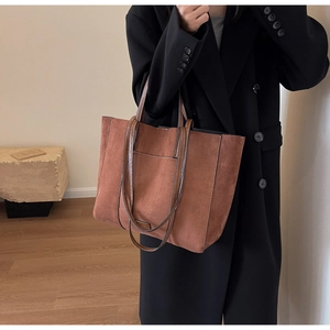 Brown vintage matte tote bag with shoulder straps worn over a long black winter coat