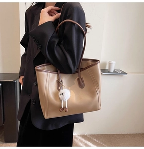 Macro detail of large khaki faux leather tote bag with stylish plush monster pendant