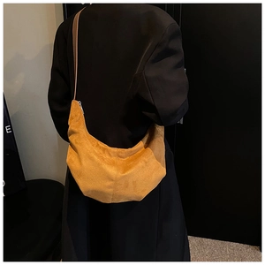 Sac bandoulière en daim jaune moutarde porté sur un manteau noir élégant pour femme