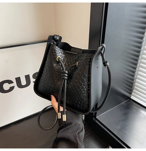 Detail of black woven leather bucket bag featuring drawstring closure and crossbody strap