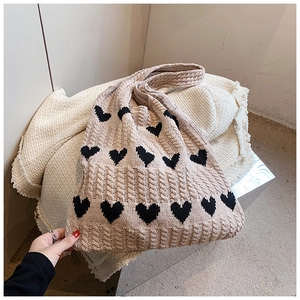 Détail de maille torsadée sur un sac fourre-tout beige avec broderie de coeurs noirs