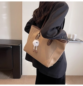 Large khaki and brown tote bag with plush monster charm shown on model's shoulder