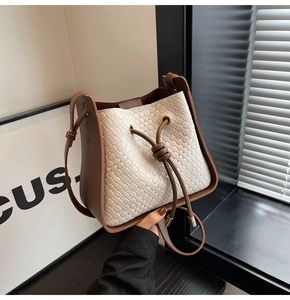 Close-up of woven bucket bag with brown leather trim and metal tipped drawstring closure