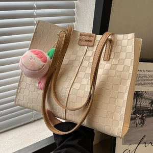 Large beige checkered tote bag with brown leather handles and a peach plush pendant