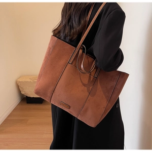 Detailed view of brown matte suede tote bag featuring metallic logo and contrast stitching