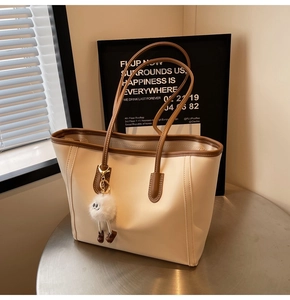 Detail of beige tote bag with brown trim featuring a cute white plush doll charm