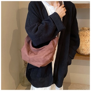Détail d'un sac bandoulière demi-lune en daim rose poudré porté par un mannequin en intérieur
