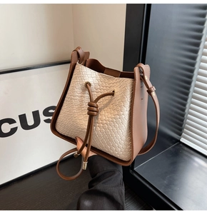 Detail of woven bucket bag with brown leather trim and golden metal drawstring tips