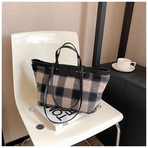 Detail of checkered canvas tote bag featuring leather handles on a minimalist white chair