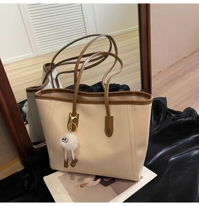 Close-up of a cream tote bag with brown handles and a cute plush monster charm
