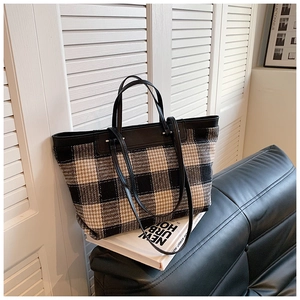 Detail of checkered woven tote bag featuring black leather handles on a leather sofa
