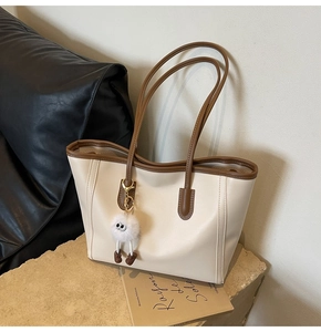 Detail of a large beige tote bag with brown trim and a cute plush ball charm on a stone base