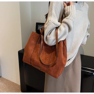Detail view of large brown frosted leather tote bag with stitch decor and metal plate