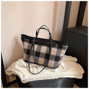 Close-up of large plaid tote bag with black leather handles on a stylish background