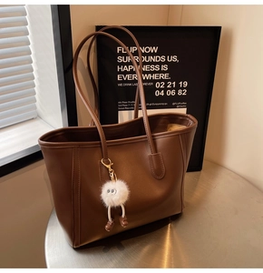 Detail of deep brown tote bag with smooth texture and cute plush doll charm