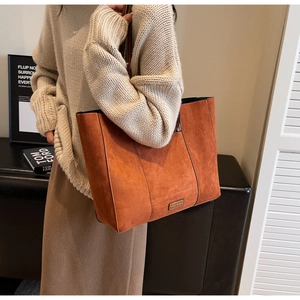 Detail view of large orange-brown suede tote bag with vertical stitching and metal logo tag