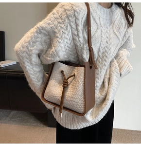Detail of a woven cream leather bucket bag with brown drawstrings and metal accents