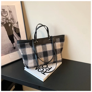 Close-up of large plaid canvas tote bag with black leather trim and metal hardware detail
