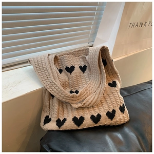 Gros plan d'un sac cabas en tricot beige avec motifs de cœurs noirs et torsades