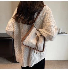 Detail of white woven bucket bag with brown leather trim worn over a white sweater
