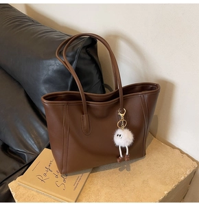 Detail of large brown faux leather tote bag featuring a cute white plush monster pendant