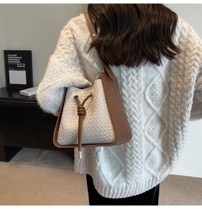 Detail of white woven bucket bag featuring brown leather trim and knotted drawstring design
