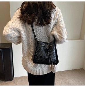 Detail view of black woven bucket bag with drawstring closure on model's shoulder