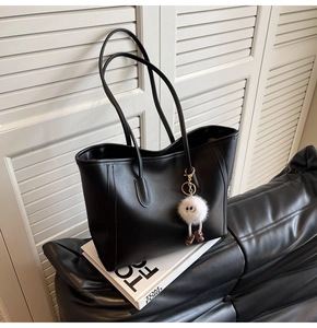 Detail shot of a black leather tote bag with a white plush doll charm on a leather sofa