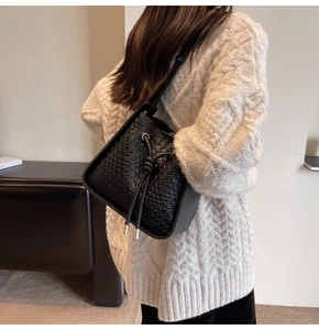 Detail of black woven texture bucket bag showing side view on white sweater background