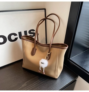 Detail of khaki tote bag featuring brown trim and a white fluffy monster charm accessory