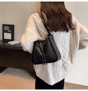 Detail of black woven bucket bag featuring large weave pattern and wide strap on model