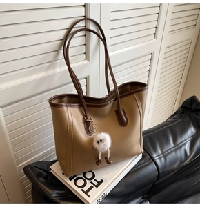 Detail view of khaki PU leather tote bag with a white plush monster charm on its side