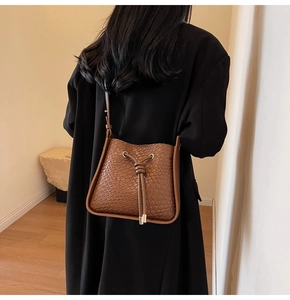 Rear view of a model wearing the brown drawstring bucket bag with woven texture details