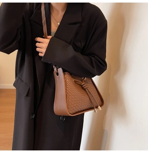 Detail of a brown woven texture shoulder bucket bag with golden metal hardware and drawstring