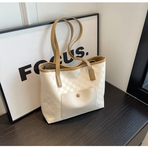 Detail of checkered tote bag with brown leather handles resting against a Focus picture frame