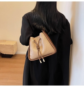 Detail view of a beige crocodile pattern bucket bag worn with a black blazer