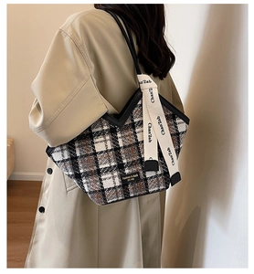 Detail of tweed tote bag with V-shaped opening and decorative ribbon on shoulder strap