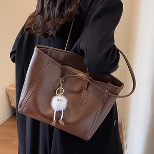 Large dark brown leather tote bag with fluffy white charm shown on model shoulder