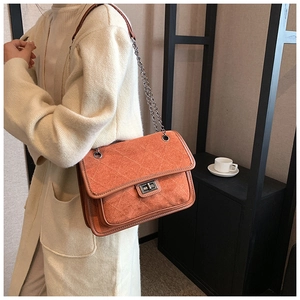 Detail of orange quilted crossbody bag with gunmetal chain strap and swivel lock