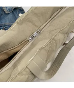 Detail of smooth silver zipper hardware on a quilted khaki nylon tote bag for women