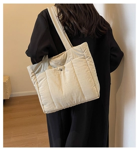 Detail of beige quilted nylon tote bag showing front magnetic pocket and wide shoulder strap