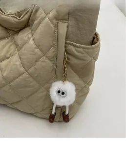 Detail of white fluffy plush charm with big eyes on khaki quilted nylon tote bag